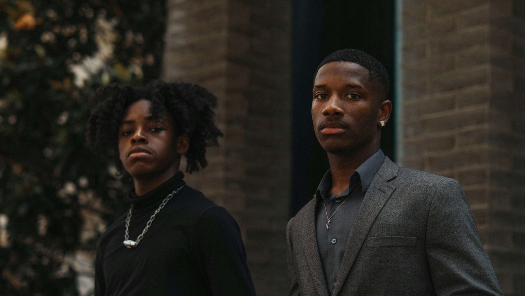Two young men standing together outside a brick building