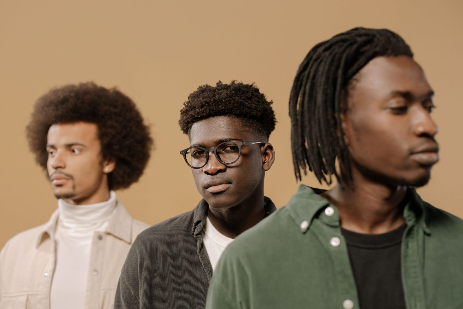 Three men standing together against a warm ochre wall