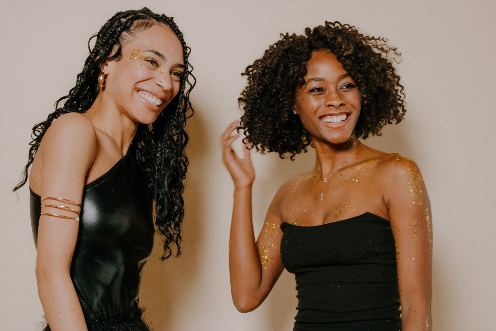 Two women laughing together against a warm wall